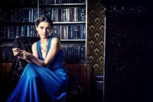 Beautiful young woman sitting in a library with a blue evening dress